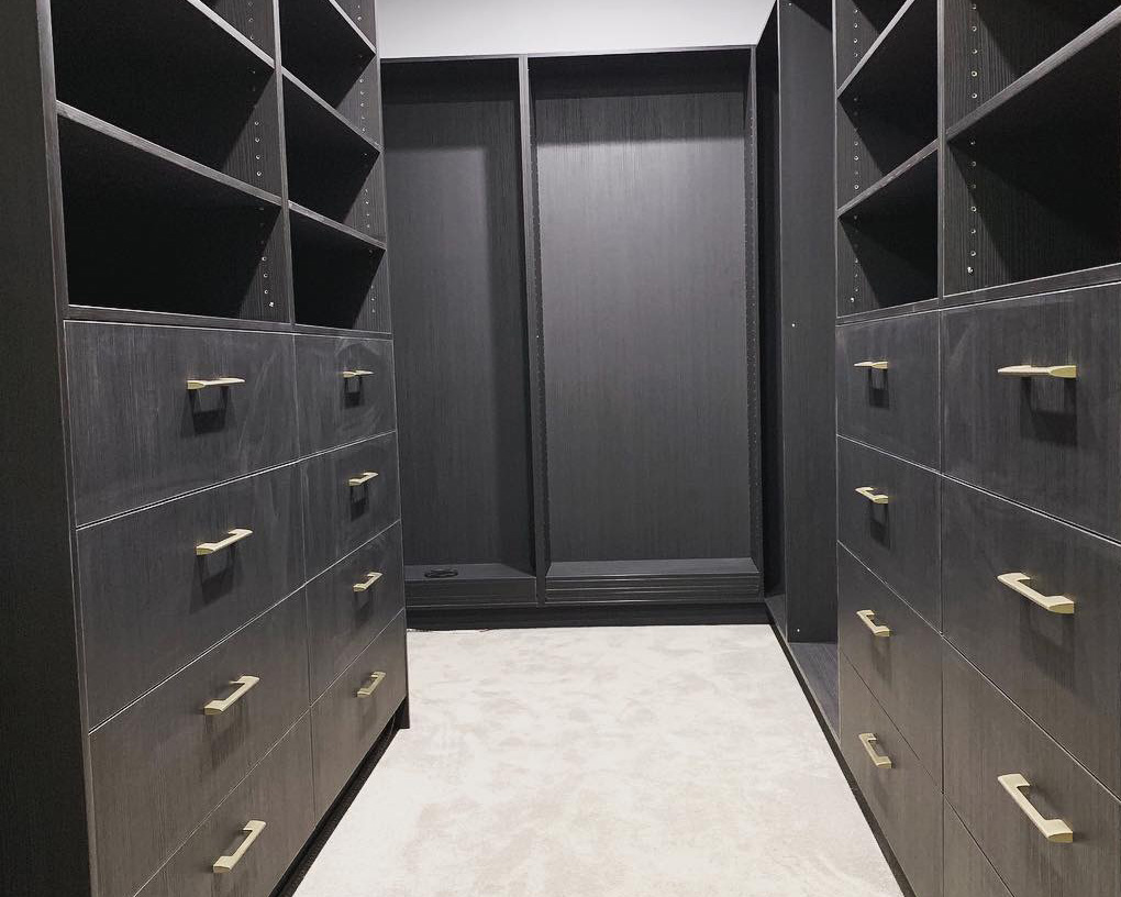 Luxurious dark wood walk-in closet with gold handles.