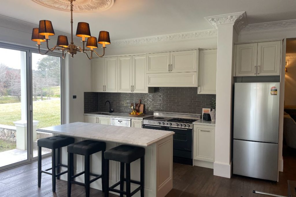 Modern kitchen with white cabinetry, marble island, and chandelier.