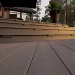 Elegant outdoor deck with a staircase made of smooth wooden planks, complemented by modern glass railings and potted plants, creating a cozy and stylish seating area surrounded by nature.