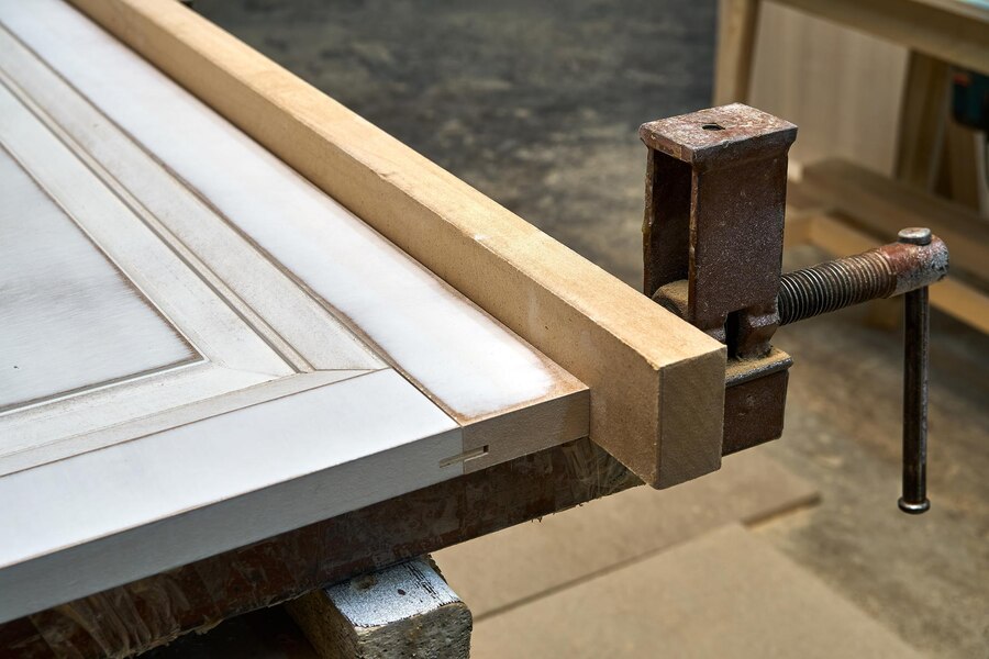 Close-up of woodworking clamp securing a wooden door frame during the joinery process, highlighting craftsmanship and precision in cabinet making and home improvement projects.