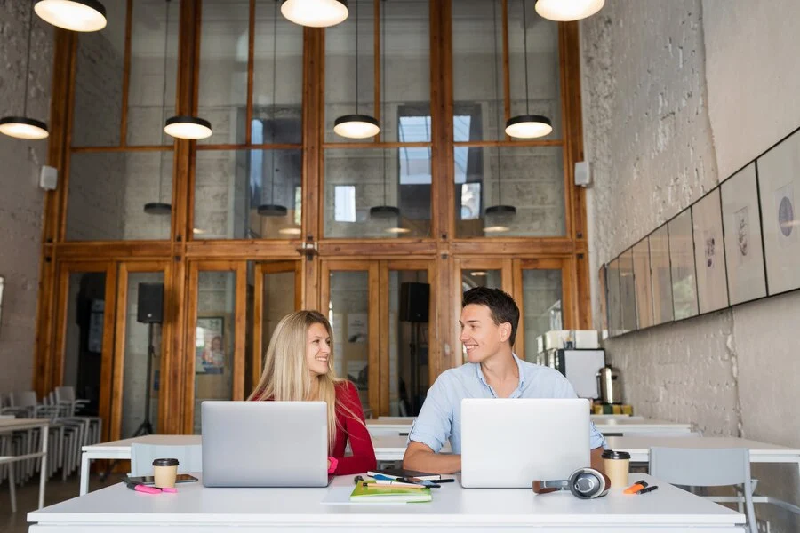 Two young professionals collaborating in a modern office space with large wooden doors and open design, highlighting workspace productivity and office furniture solutions. Ideal for coworking, office layout ideas, and contemporary workspace design.