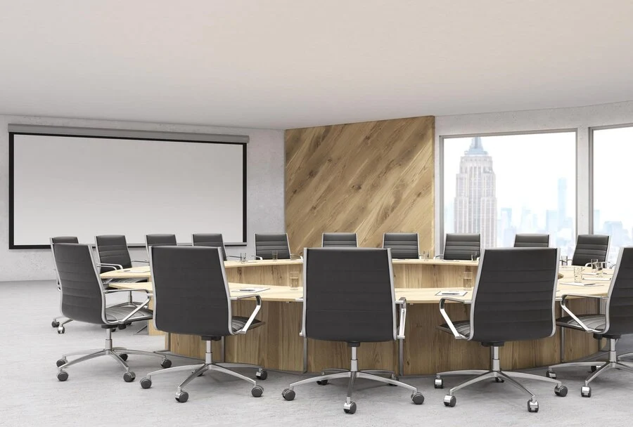 A modern conference room featuring a round wooden table with sleek black swivel chairs arranged around it. The room includes large windows with a cityscape view and a wooden accent wall that adds warmth to the space. A projector screen is mounted on the opposite wall, showcasing the room's functionality for meetings and presentations. The design reflects a professional and sophisticated atmosphere.