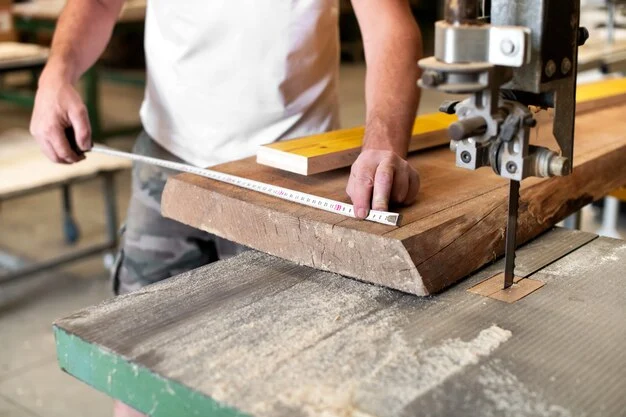 A person measuring a large wooden plank with a tape measure in a woodworking shop. The plank is positioned on a bandsaw table, ready for precise cutting. The scene highlights craftsmanship and precision in joinery work