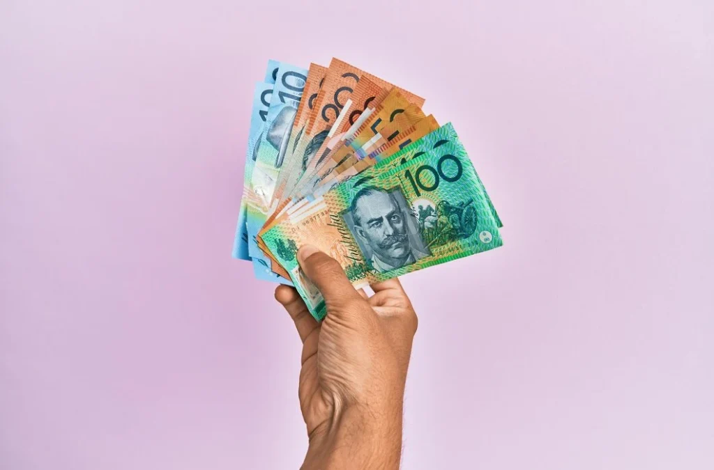 Hand holding Australian banknotes ($100, $50, $20) on light purple background.