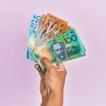 Hand holding Australian banknotes ($100, $50, $20) on light purple background.