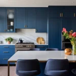 Navy kitchen: gold handles, marble backsplash, steel oven. Island with flowers, blue chairs.