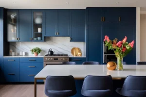 Navy kitchen: gold handles, marble backsplash, steel oven. Island with flowers, blue chairs.