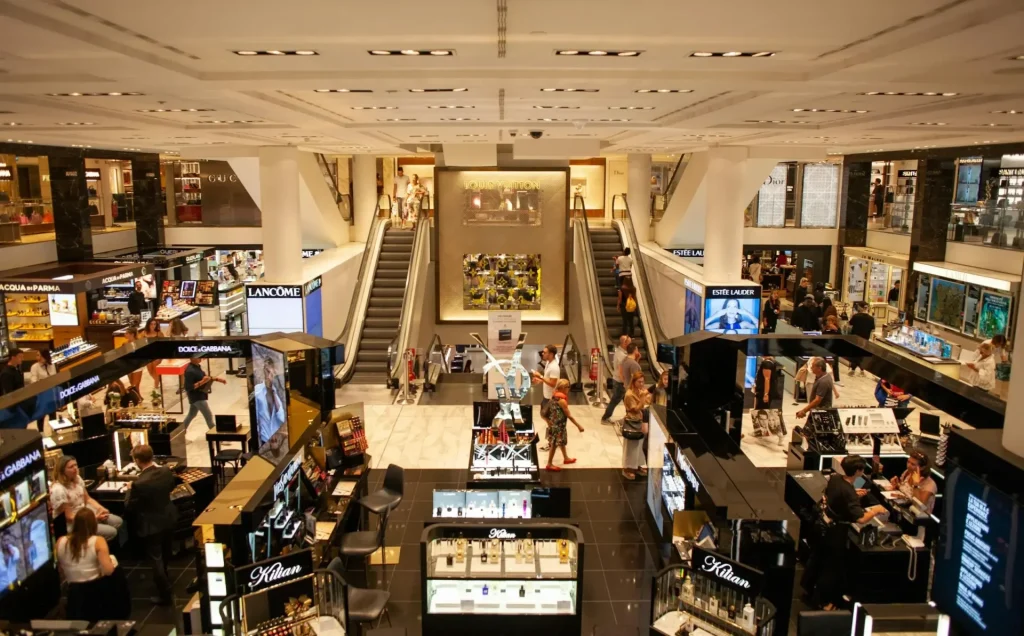 Upscale store: brand displays, escalators, shoppers. Modern, luxury feel.